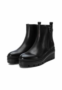 Botas de tobillo de cuero negro con una suela de tracción gruesa, cremallera lateral y lengüeta. Textura suave con acentos mínimos y un diseño elegante.