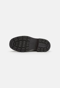 Semelle de chaussure en caoutchouc noir avec une surface texturée présentant de profondes rainures et motifs pour l'adhérence. Les marquages incluent la taille 37 et le logo de la marque.