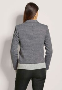 Blazer aus einem strukturierten Stoff in Schwarz und Weiß mit einem grauen, gerippten Stricksaum. Verfügt über einen klassischen Kragen und lange Ärmel. Rückansicht dargestellt.