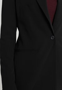 Black blazer with a single button closure, notch lapels, and side pockets. Features a smooth texture and fitted design.