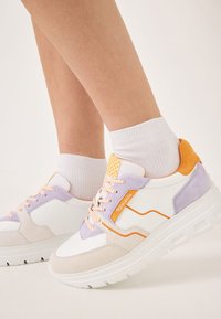 White sneakers with purple, orange, and beige accents. Made of leather and suede, featuring lace closure and textured heel detail.