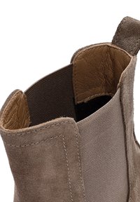 Stivale in suede alla caviglia con interno in cuoio marrone e fodera in tessuto marrone. Presenta un design cucito e un tassello sul retro per una facile calzata.