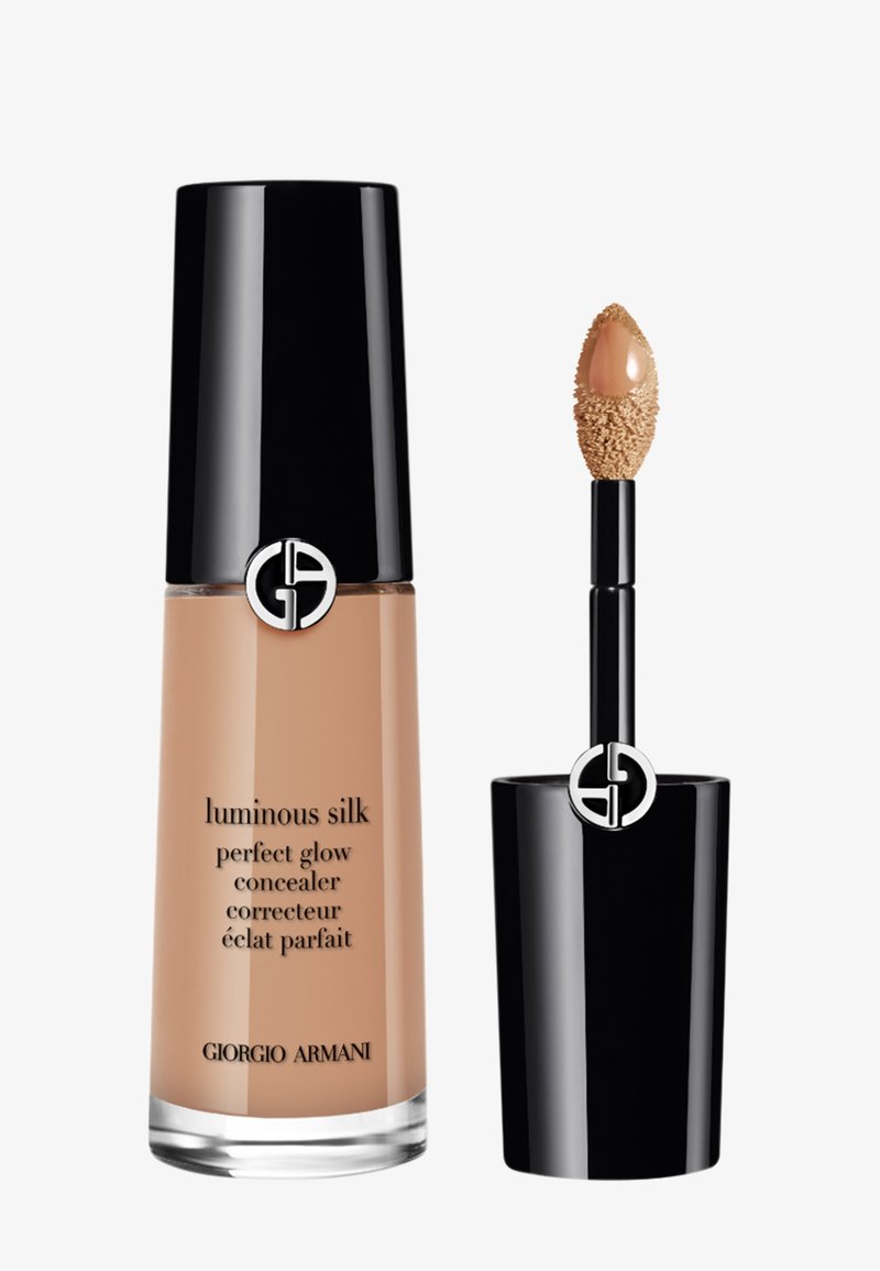 Luminous Silk Perfect Glow Concealer i en klar glassflaske med svart lokk. Inkluderer en doe-foot-applikator med et brunt produkt på spissen.