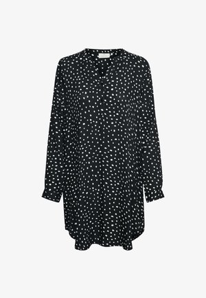Tunique noire à manches longues avec des pois blancs irréguliers, un col en V avec trois boutons et des manches avec poignets.