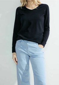 Svart långärmad stickad tröja tillsammans med ljusblå jeans. Tröjan har en rund halsringning; jeansen har fickor och en avslappnad passform.