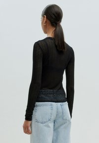 Schwarzes Netz-Oberteil mit langen Ärmeln, gerippter Textur, enger Passform und einem subtilen Glanz, kombiniert mit hochtaillierten hellblauen Jeans.