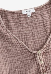 Light pink, textured fabric top with a V-neck and button closure. Patterned with small raised dots and a woven grid design. Label visible.
