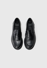 Zwarte leren loafers met een krokodillenprint, ronde neus en een band over de wreef. Gladde binnenvoering met minimale branding.