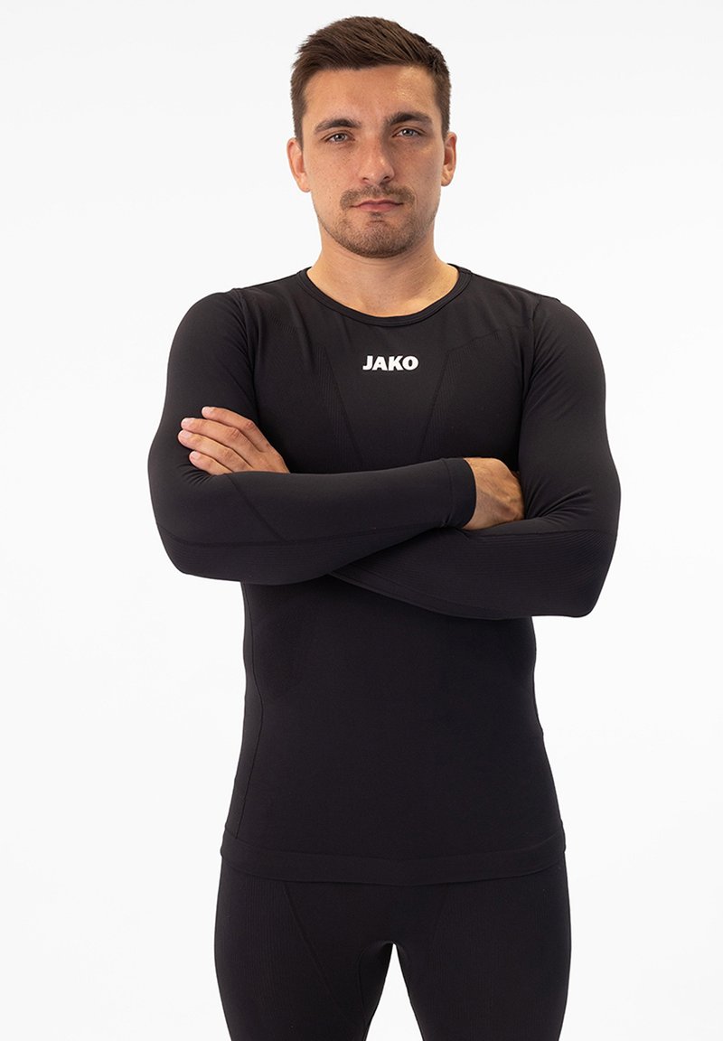 Maglietta a compressione nera a maniche lunghe con collo rotondo, realizzata in materiale elasticizzato, con dettagli testurizzati e logo "JAKO" bianco sul davanti.