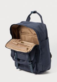 Marinblå kanvasryggsäck med ett framflap, beige insida, dragkedjefack och justerbara remmar. Har ett handtag upptill för bärande.