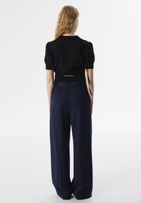 Top nero a maniche corte con spalline sopra un paio di pantaloni larghi blu scuro, con tasche laterali e una finitura liscia.