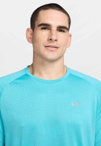 Camisola atlética turquesa com um padrão texturizado, decote arredondado e mangas curtas. Possui um pequeno logótipo prateado da Nike no peito.