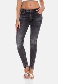 Schwarze, hochgeschnittene Skinny-Jeans mit ausgewaschenem Finish, kontrastierenden Nähten und Fünf-Taschen-Design. Kombiniert mit weißen, Riemchensandalen.