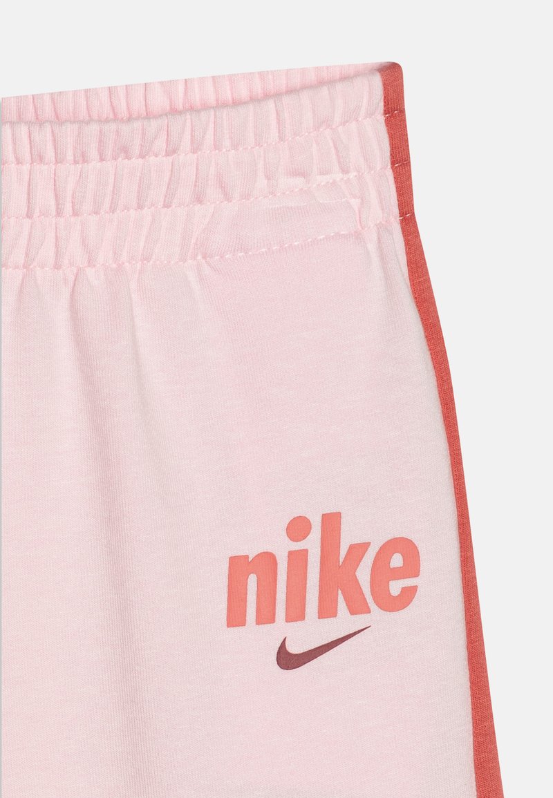 Shorts Nike rose clair avec une taille élastique et une bande latérale orange, arborant le logo et le swoosh Nike en orange et bordeaux.