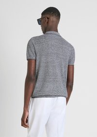 Polo shirt grigio a maniche corte con finitura a maglia testurizzata, dotato di colletto classico e orlo dritto, indossato con pantaloni bianchi.