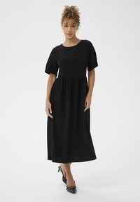 Vestido midi negro de manga corta y texturizado, con un cuerpo ajustado y una falda abullonada. Llevado con tacones negros de tiras con punta.