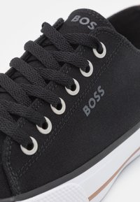 Basket en toile noire avec lacets noirs, œillets en métal et logo "BOSS" sur le côté et sur la languette, avec une semelle en caoutchouc blanche comportant une bande marron.