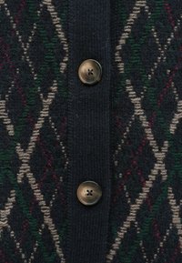 Cardigan marine présentant un motif en losange beige, vert et rouge, avec trois grands boutons marron à l'avant. Texture tricotée visible.