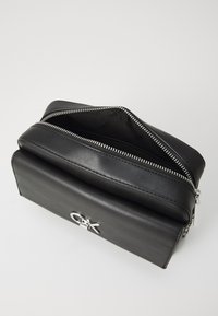 Borsa in pelle nera a forma rettangolare, con chiusura a zip argentata e accento con logo. Interno foderato in tessuto e spazioso.