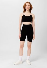 Top corto nero e pantaloni da ciclista a vita alta realizzati in tessuto morbido. Modella che indossa sneakers bianche e calzini alla caviglia. Design semplice e aderente.
