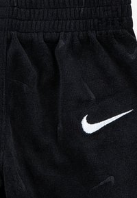 Μαύρο παντελόνι από φλις με ελαστική ζώνη μέσης και λευκό κεντητό λογότυπο Nike στο αριστερό μηρό, που παρουσιάζει μια απαλή υφή.