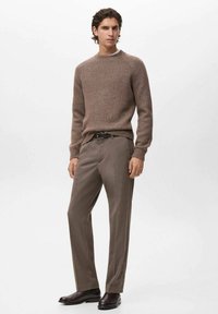 Hnědý svetr s textura a kulatým výstřihem je spárován s béžovými elegantními kalhotami. Černý opasek a tmavé boty dotvářejí outfit.