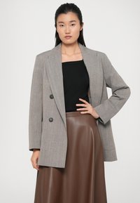 Gray plaid double-breasted blazer with notched lapels and two buttons, paired with a black top and brown leather-like midi skirt.