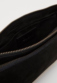 Černý velurový sáček se zipovým uzávěrem, s měkkým interiérem a malou černou štítkou uvnitř. Texturovaný povrch, minimalistický design.