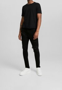 Camiseta de algodón negra, de manga corta, con cuello redondo, combinada con jeans skinny negros desgastados y zapatillas blancas. Conjunto simple y casual.