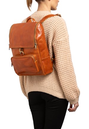 Zaino in pelle marrone con una forma strutturata, un coperchio superiore, una tasca frontale e spallacci regolabili, indossato da una persona con un maglione beige.