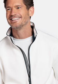 Witte ritssluitingjack met een hoge kraag, voorzien van zwarte rand en een gladde textuur. Draag boven een wit shirt met ronde hals.