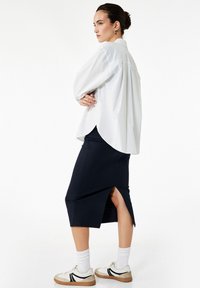 Witte oversized button-up shirt met lange mouwen, gecombineerd met een marineblauwe kokerrok met een zijnaad. Witte sokken en sneakers maken de look compleet.