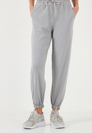 Lichtgrijze joggingsbroek met een elastische tailleband, details met trekkoord, zijzakken en elastische boorden. Gekoppeld met grijze sneakers.