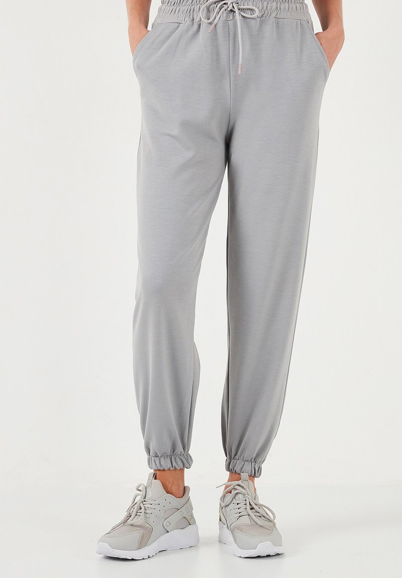 Helle graue Jogginghosen mit elastischem Bund, Kordelzug, Seitentaschen und elastischen Bündchen. Kombiniert mit grauen Turnschuhen.