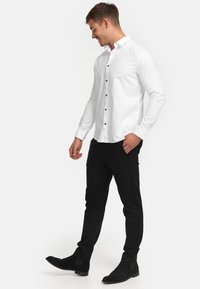 Weißes Langarmhemd mit Knopfleiste, schwarze schmal geschnittene Hose und schwarze Wildleder-Ankle Boots, die eine glatte Textur und ein gut geschnittenes Design aufweisen.