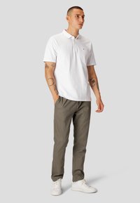 Hvid polo t-shirt med korte ærmer og krave, parret med olivengrønne bukser og hvide sneakers. Simpelt design, afslappet pasform.