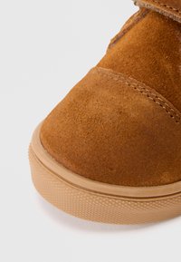 Brauner Wildlederstiefel mit runder Zehenpartie, genähten Akzenten und einer strukturierten Gummisohle. Das Obermaterial hat eine weiche Oberfläche und ein Design mit niedrigem Knöchel.