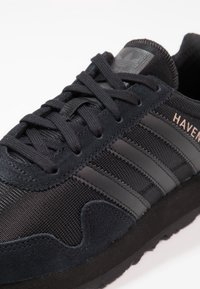 Mustat tennarit, joissa on verkko- ja mokkanahkamateriaaleja. Mallissa on kolme sävyä oleva raita ja kuvioitu kumipohja.