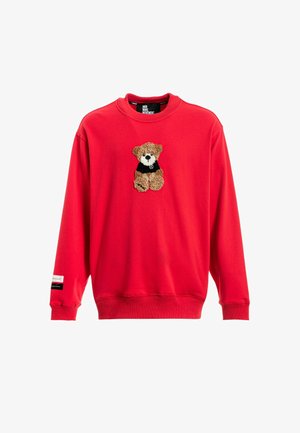 Sudadera roja con puños y dobladillo acanalados. Presenta un aplique de oso marrón texturizado en la parte frontal, vistiendo una pequeña camiseta negra.