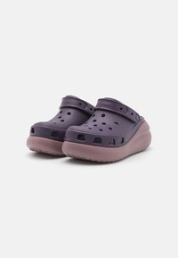 Sabots violets avec un dessus texturé, des trous de ventilation et une sangle. La semelle est d'une teinte plus claire, offrant un design rembourré.