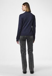 Mørkeblå genser med lange ermer, ribbestrikket halslinning og strukturert strikket stoff, sammen med høyhallet svarte jeans.