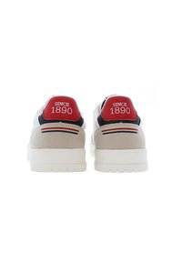 Vita sneakers med röda och svarta detaljer, mockahäl, tjock vit sula och "SINCE 1890"-detalj på hällappen.