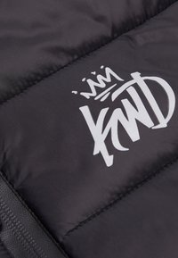 Tela acolchada negra con costuras horizontales, que presenta un logo blanco destacado. El material parece suave con un ligero brillo.