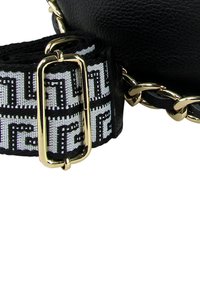 Sac en cuir noir avec une bandoulière à motif blanc et noir. Des accents en métal doré et un détail chaîne complètent la bandoulière.