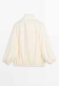 Off-white, lange mouw jas met hoge kraag, elastische boorden en zoom, van achteren getoond tegen een witte achtergrond.