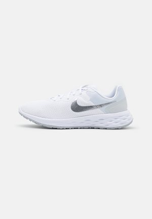 Baskets de course blanches avec une tige en mesh, des accents argentés et une semelle épaisse et rembourrée. Présente un logo Nike gris sur le côté.