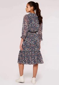 Blumenkleid mit langen, transparenten Ärmeln und einem gestuften Rock. Marineblau, Rosa und Weiß; leichtes Material mit einem Rüschensaum.