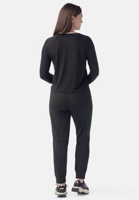Camiseta de manga larga negra y pantalones jogger negros con un ajuste ceñido, con puños acanalados y bolsillos laterales. Llevado con zapatillas negras y grises.