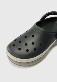 Black plastic clog with multiple ventilation holes, a rounded toe, and a white outsole. Features a back strap for a secure fit.
