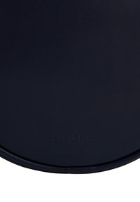 Tumši zila apaļa ādas somiņa ar smalki izgriezto "FABLE ENGLAND" logotipu pie apakšējās malas.